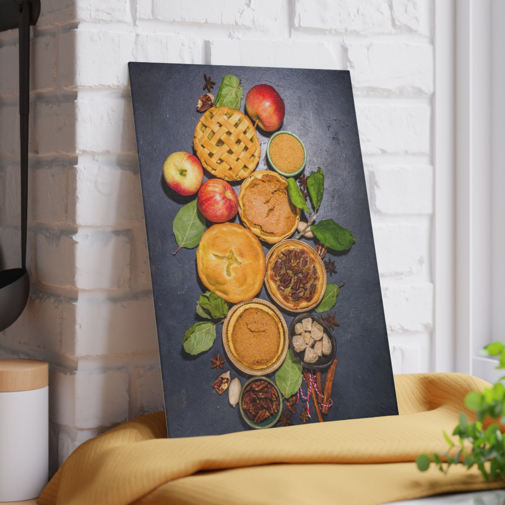Canvas print of pies and apples on a dark background, leaning against a white brick wall.