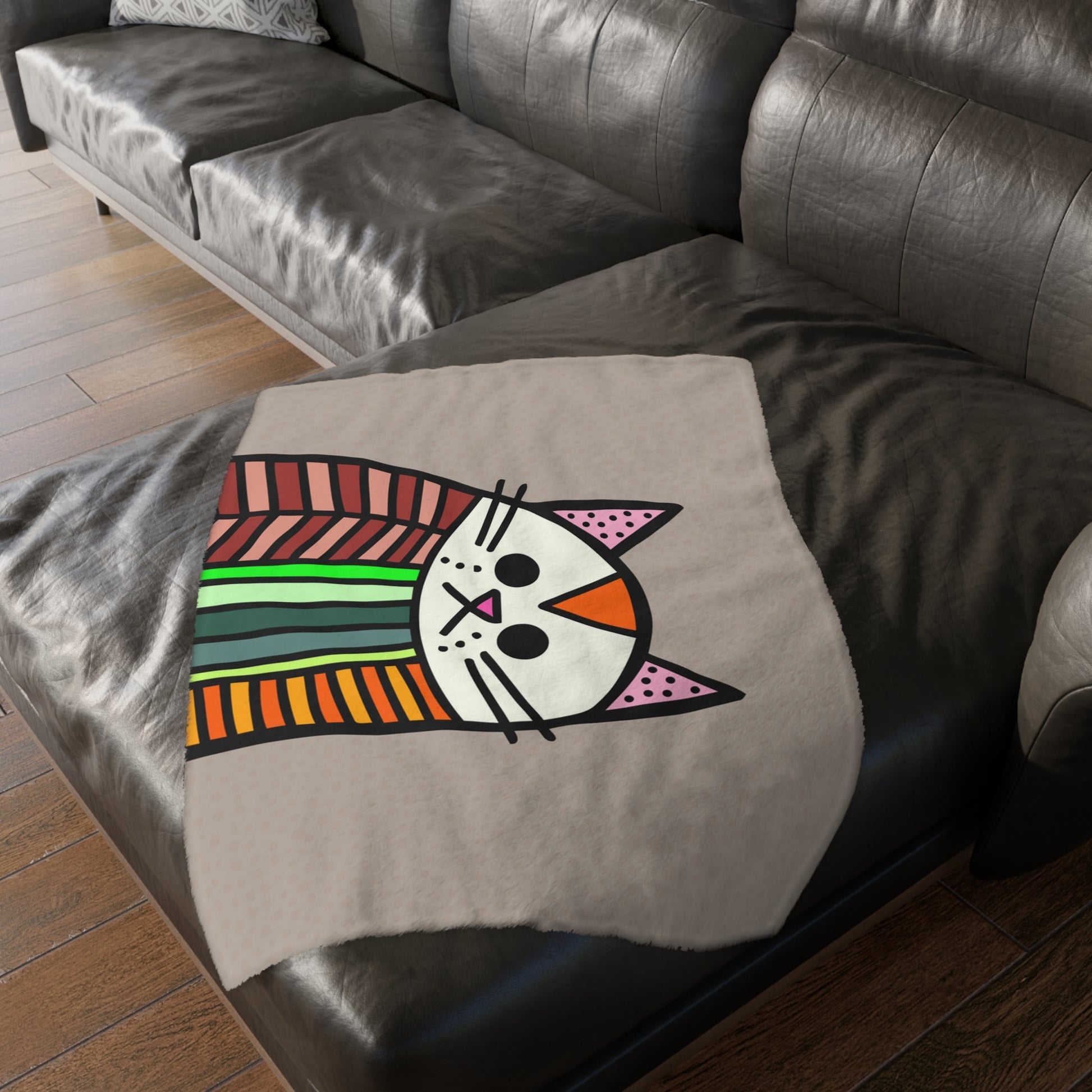 Colorful cat design on a gray blanket draped over a dark brown sofa.
