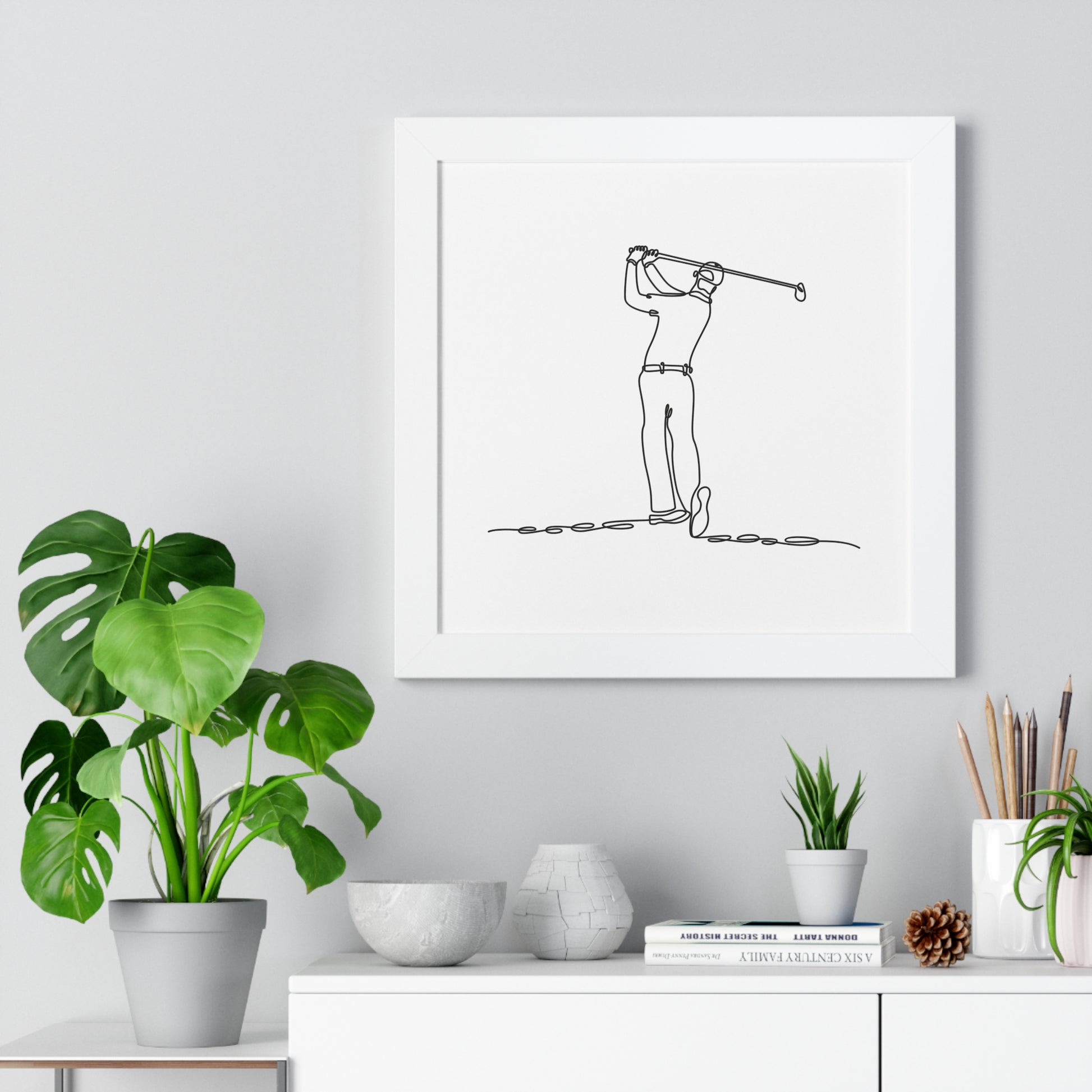 Framed artwork of a golfer in a modern interior setting with plants and decor.