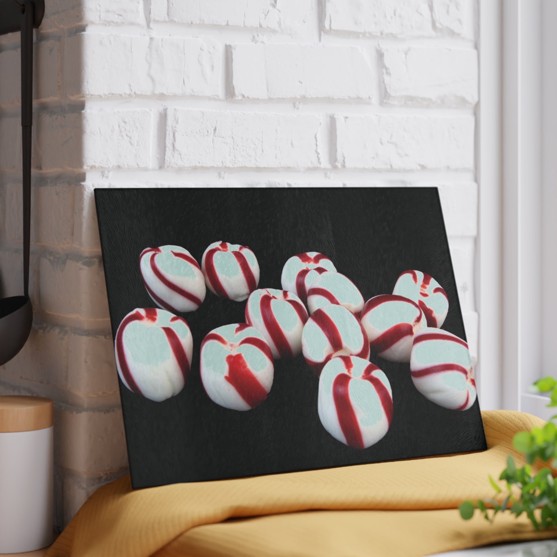 Glass cutting board red and white striped candies on a black background, leaning against a white brick wall.