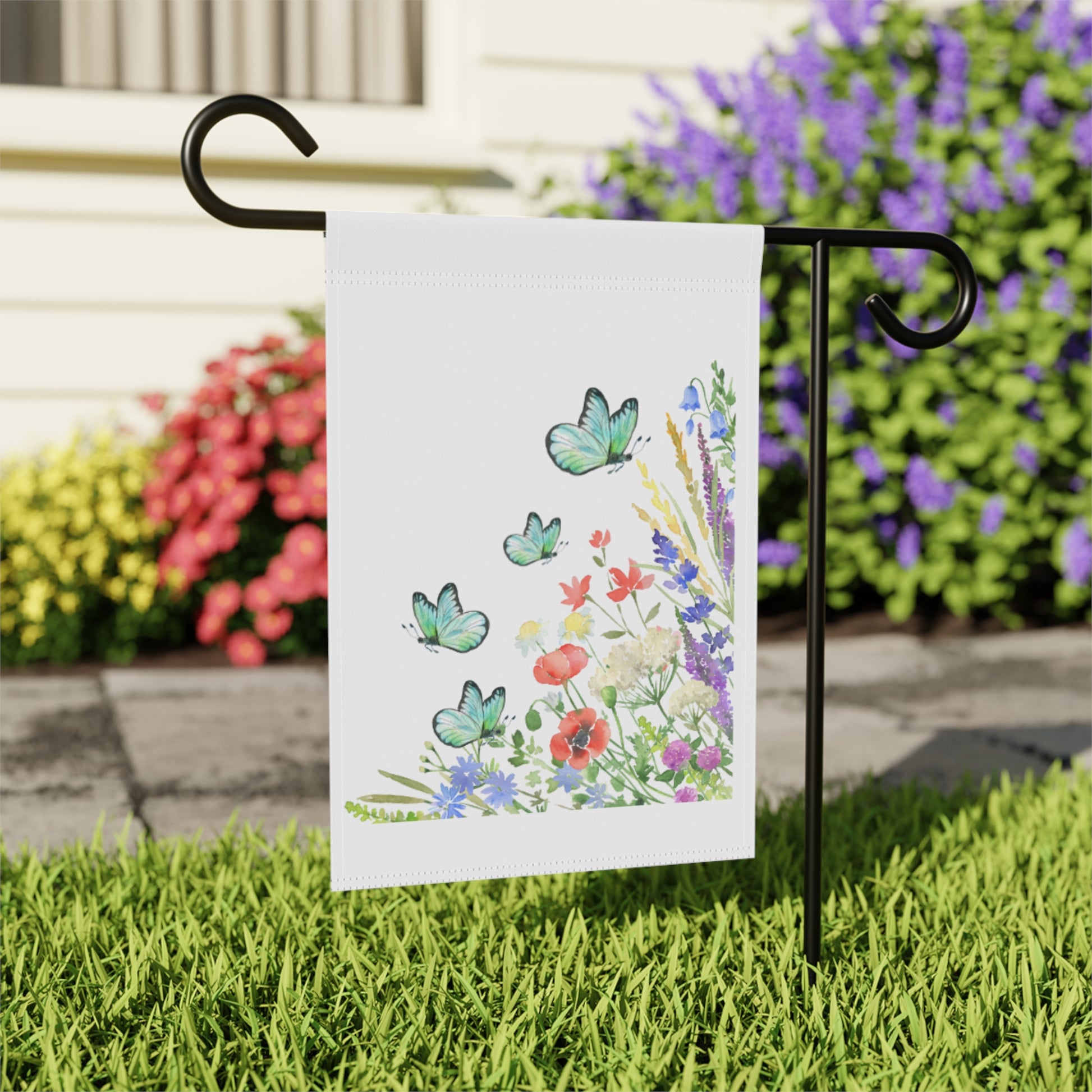 Decorative garden flag with butterflies and flowers on a stand in front of colorful flowers.