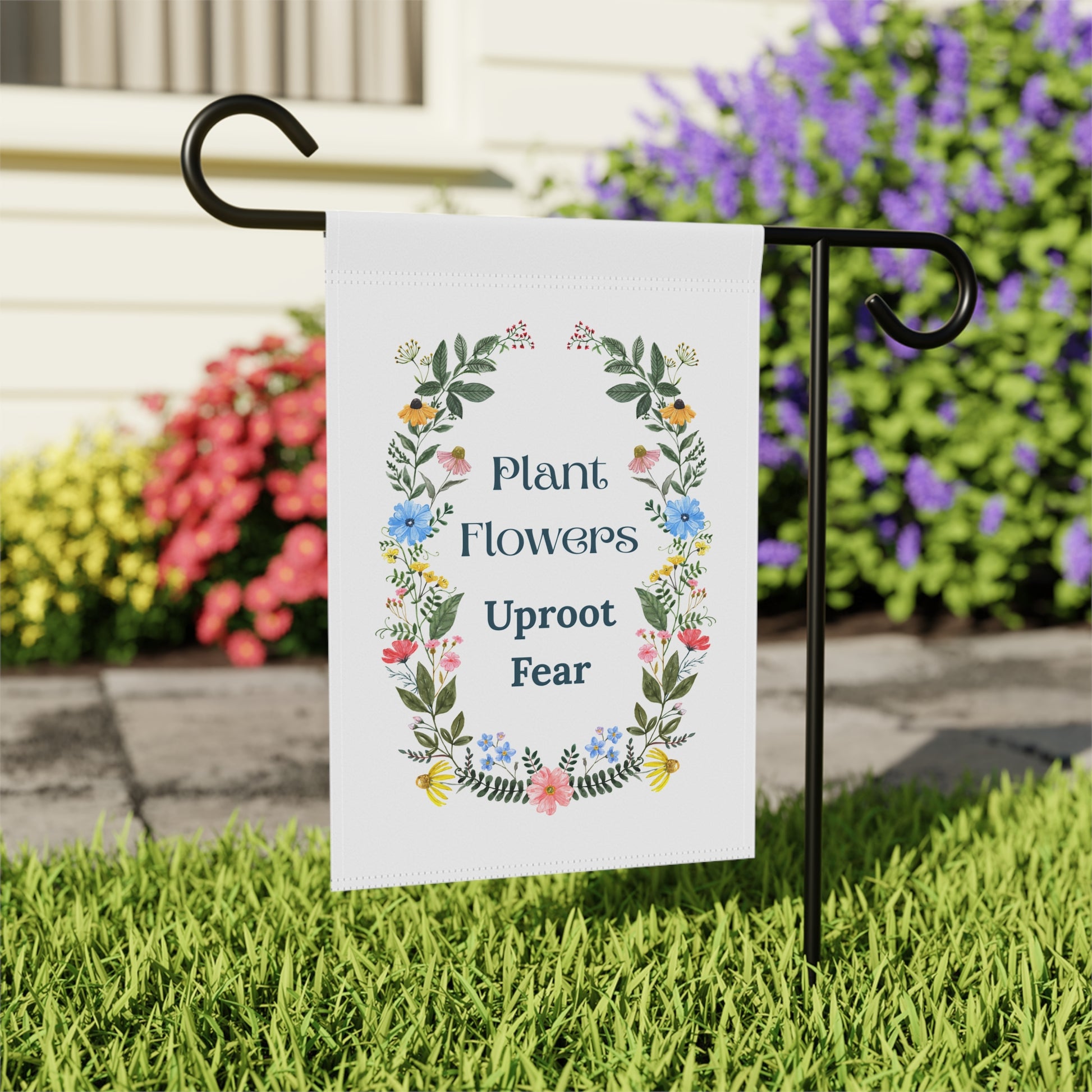 Decorative garden flag with floral design and motivational quote on a grassy lawn.