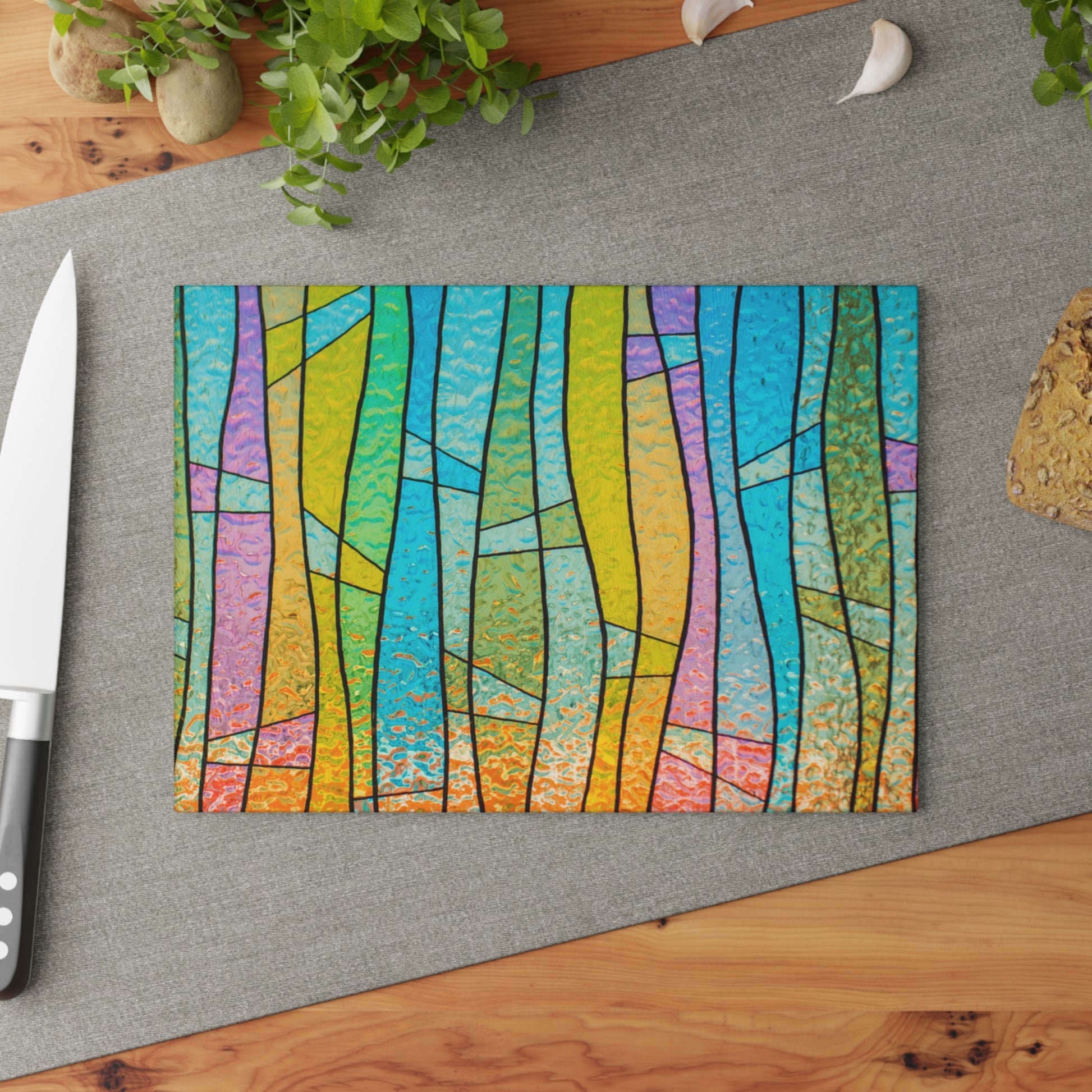 Colorful abstract design on a cutting board with a knife and plant in the background.