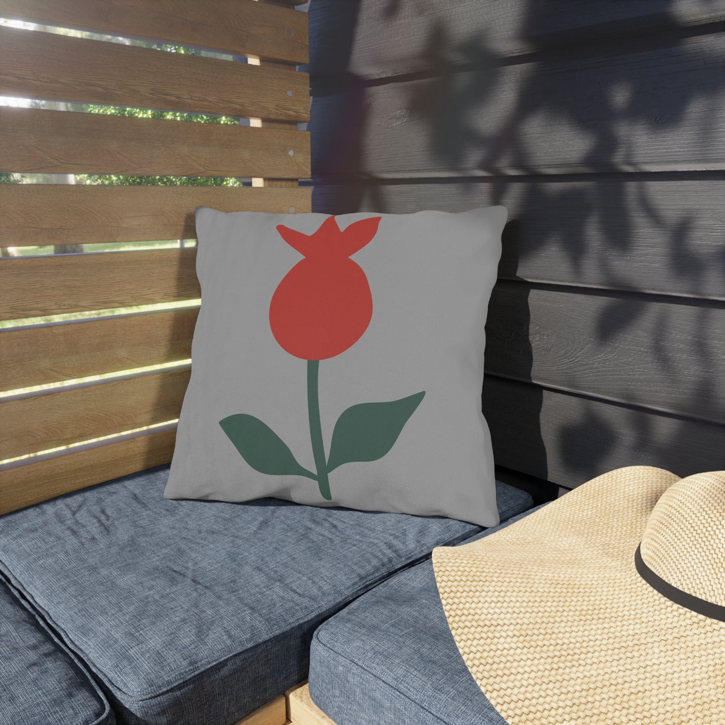 Gray pillow with a red flower design on a wooden bench