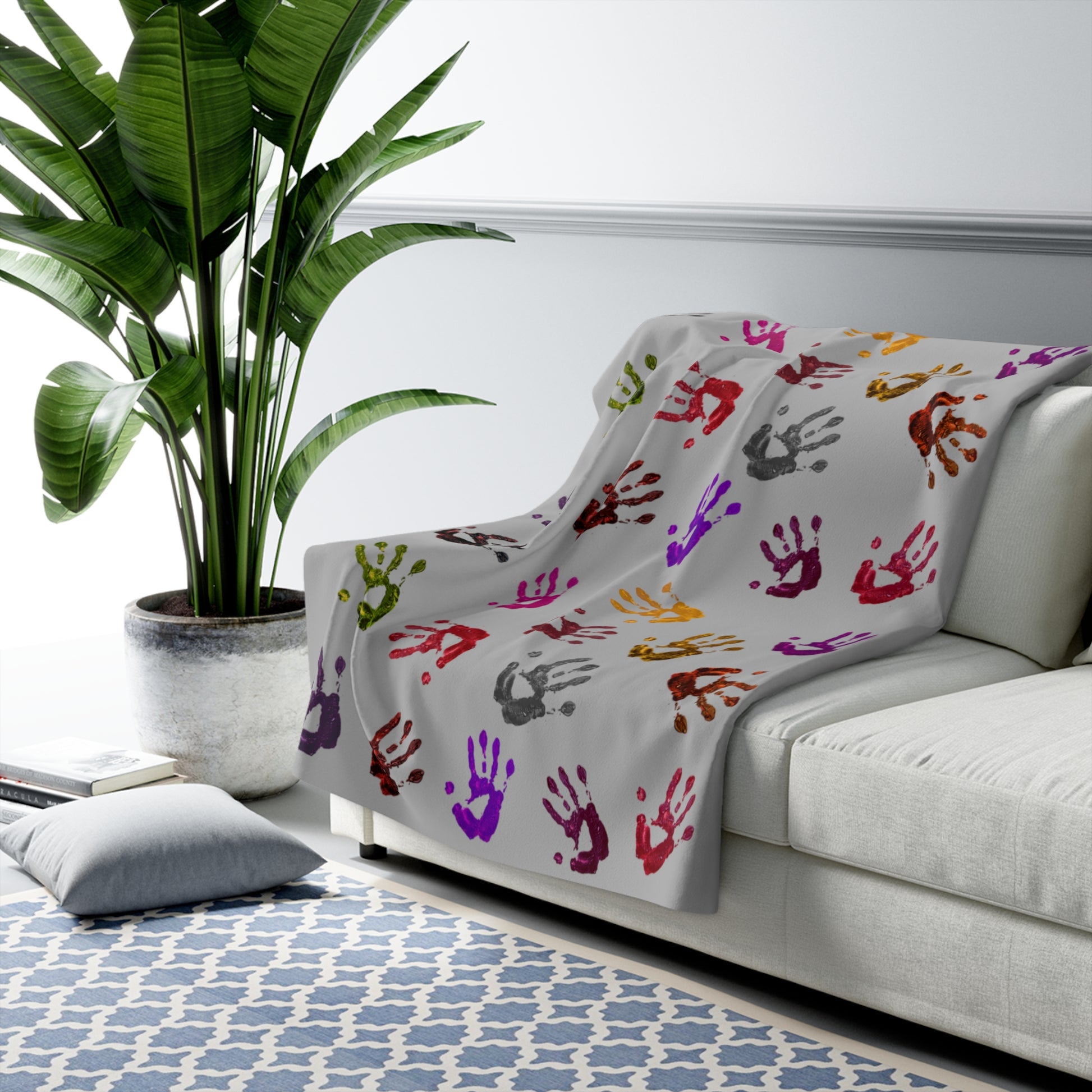 Colorful handprint blanket draped over a sofa in a living room setting with a plant and rug.