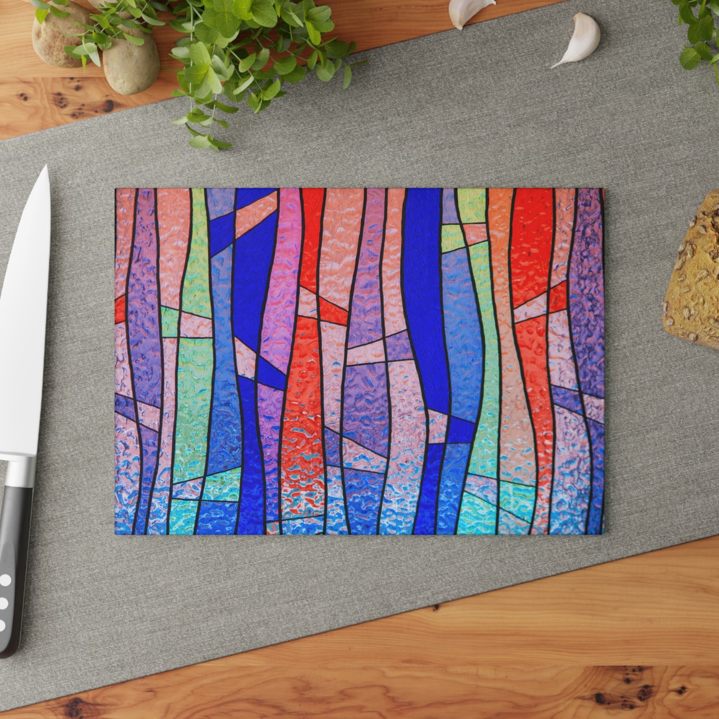 Colorful abstract design on a cutting board with a knife and plant in the background.