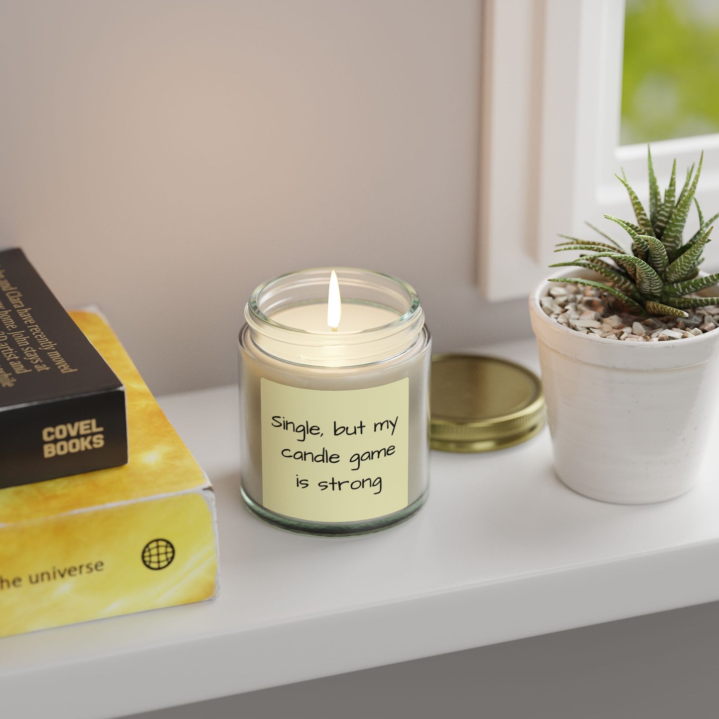 Candle with a humorous label on a shelf with a book and plant