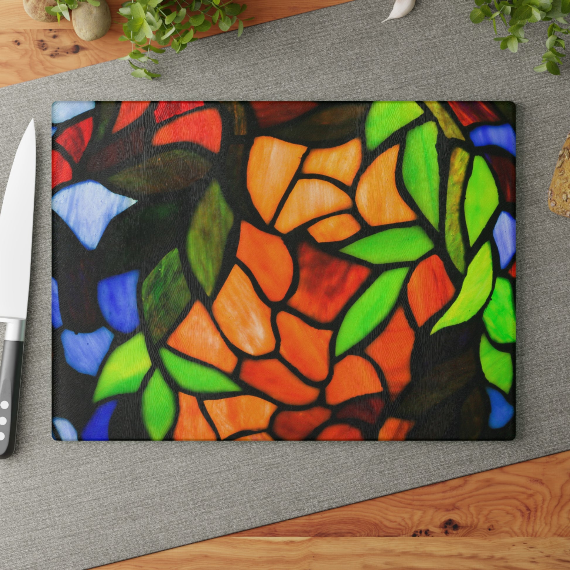 Colorful stained glass-style cutting board on a gray surface with a knife.
