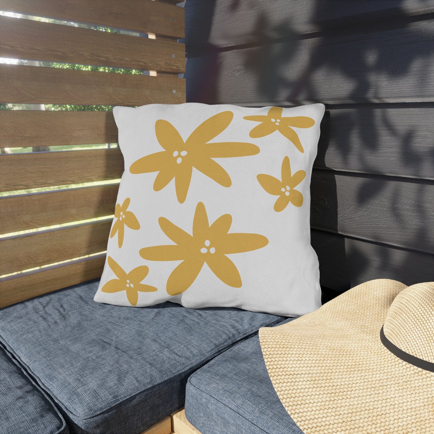 White pillow with yellow floral patterns on a gray cushioned bench outdoors.