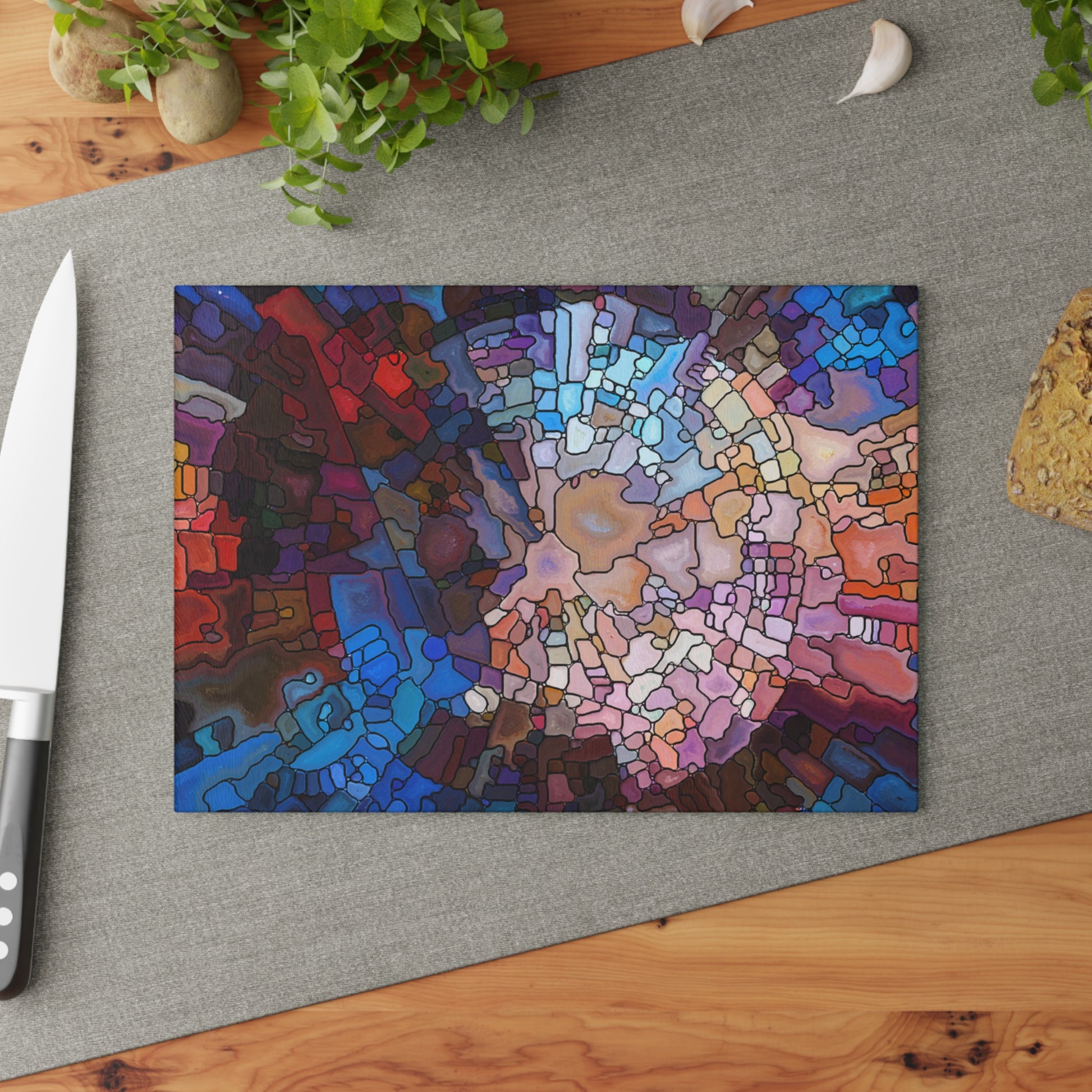 Colorful abstract design on a cutting board with a knife and plant in the background.