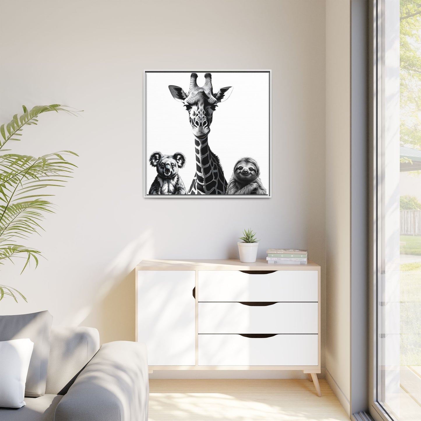 Framed artwork of a giraffe and sloths on a wall above a white cabinet.