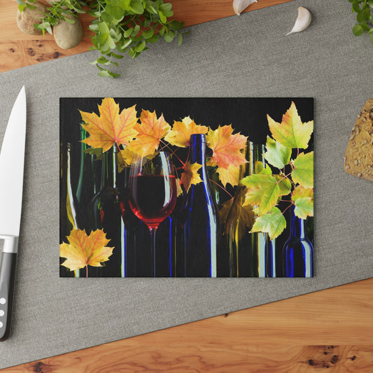 Decorative glass cutting board with autumn leaves and wine bottles on a gray surface.