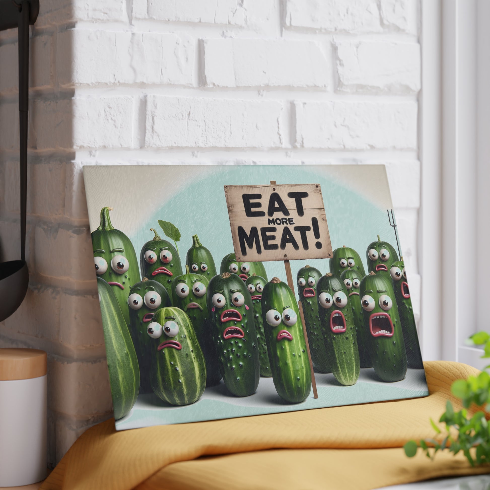 Canvas print with cartoon cucumbers holding a 'Eat More Meat!' sign against a white brick wall.