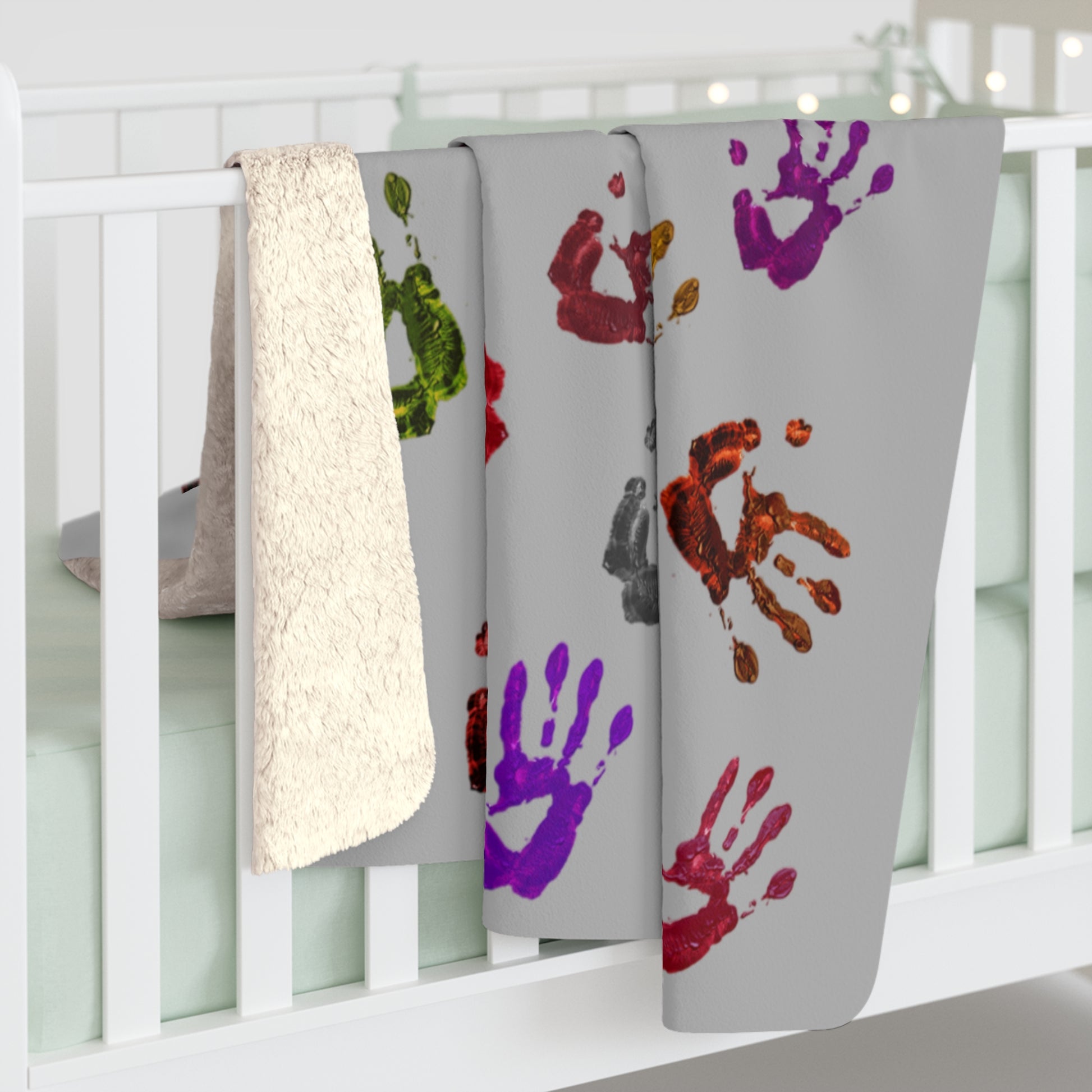 Gray blanket with colorful handprints on a white crib