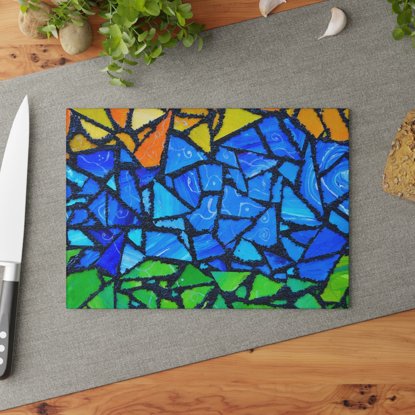 Colorful mosaic cutting board on a gray surface with a knife and plant in the background.