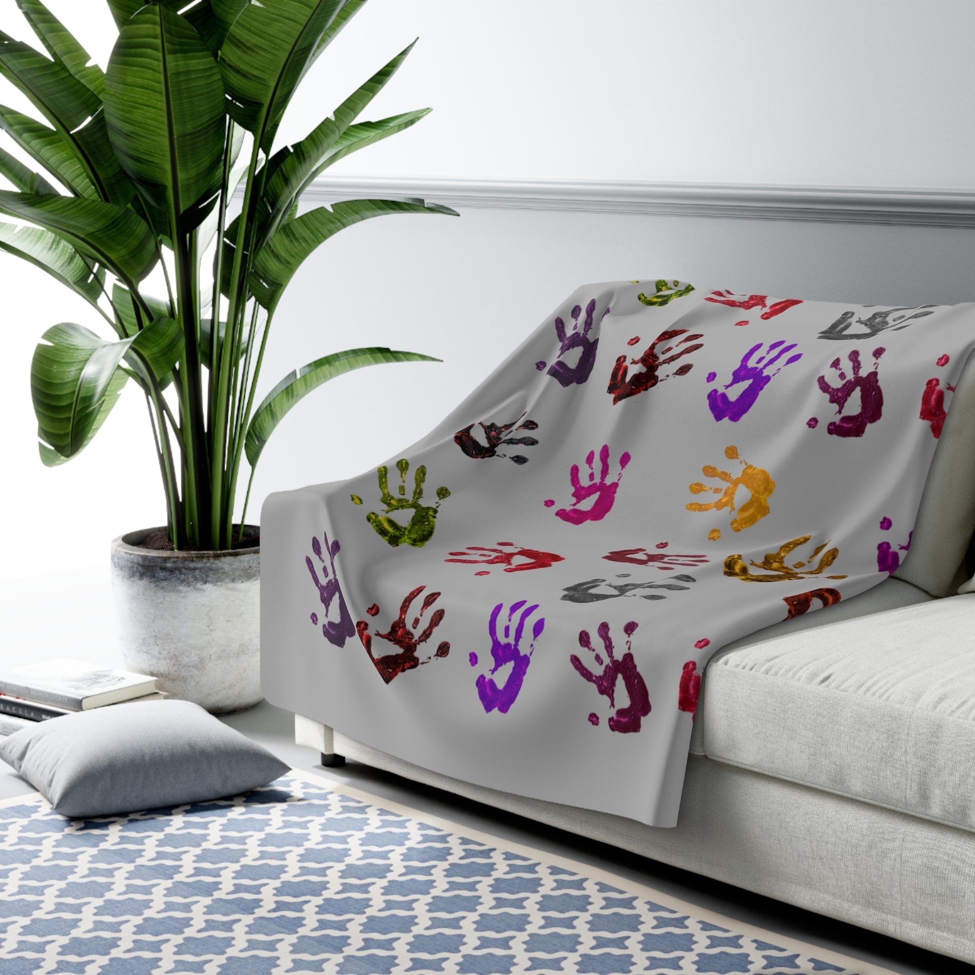 Colorful handprint blanket draped over a sofa in a living room setting with a plant and rug.