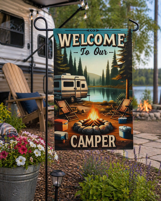 Decorative garden flag with camping scene and 'Welcome to Our Camper' text, displayed outdoors.