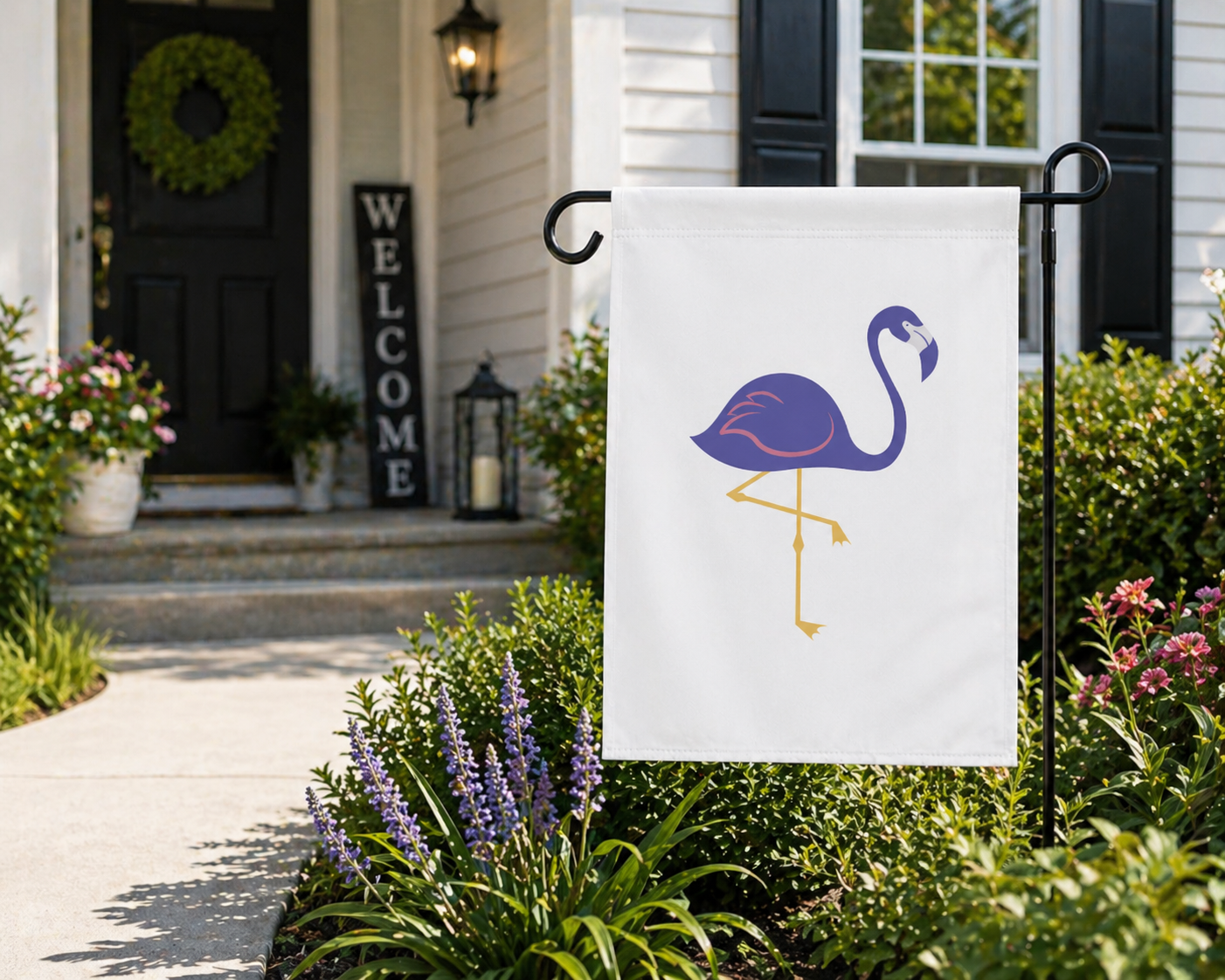 Flamingo-themed garden flag in front of a house with 'Welcome' sign and plants.