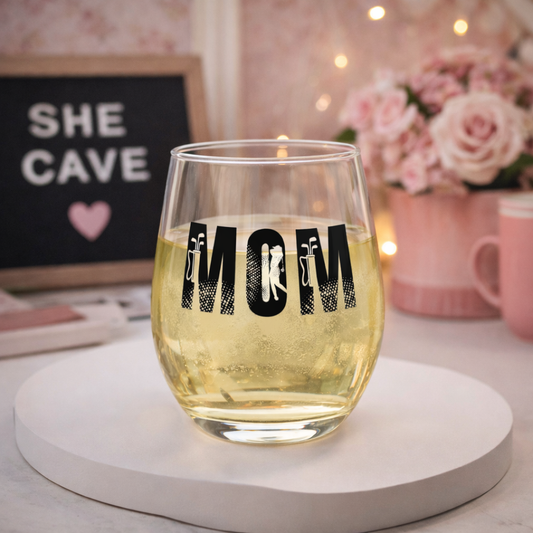 Glass of white wine with 'Mom' design on a table with decorative items in the background.