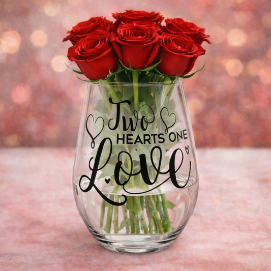 Clear glass vase with red roses and 'Two Hearts One Love' text on a blurred background