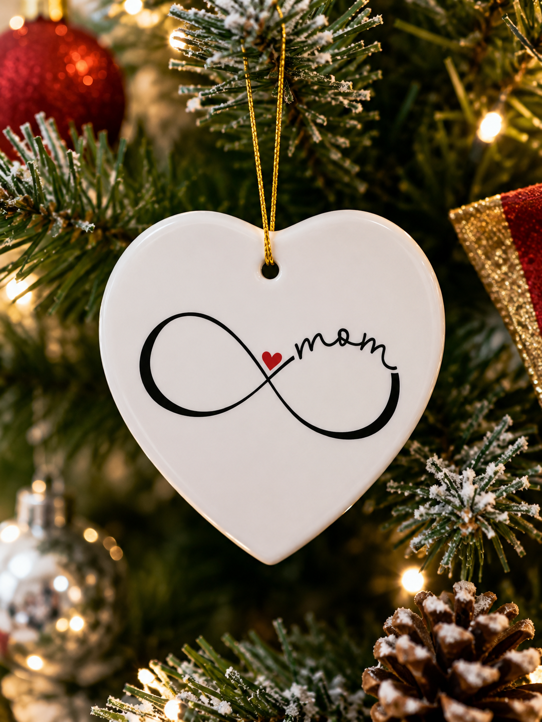 Heart-shaped ornament with 'mom' and infinity symbol hanging on a Christmas tree.