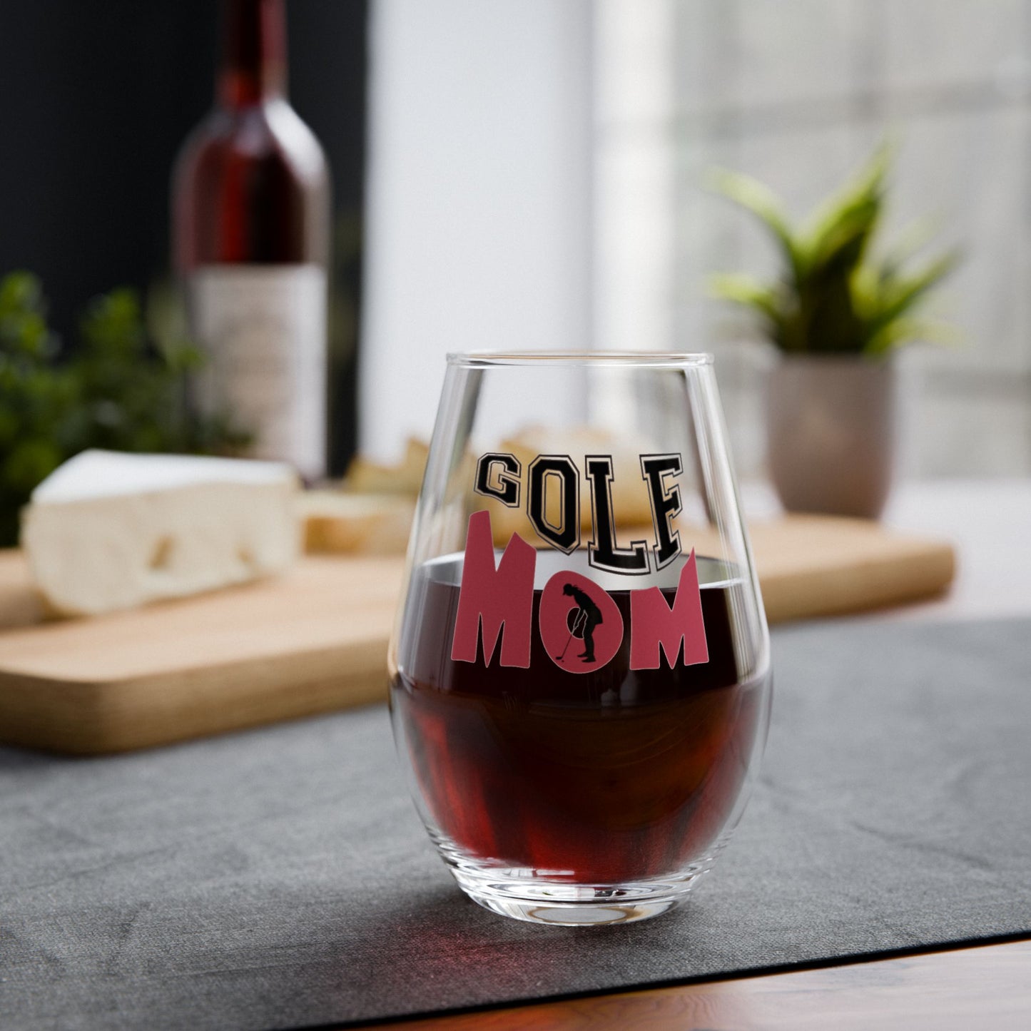 Clear wine glass with 'GOLF MOM' text filled with red wine on a table.
